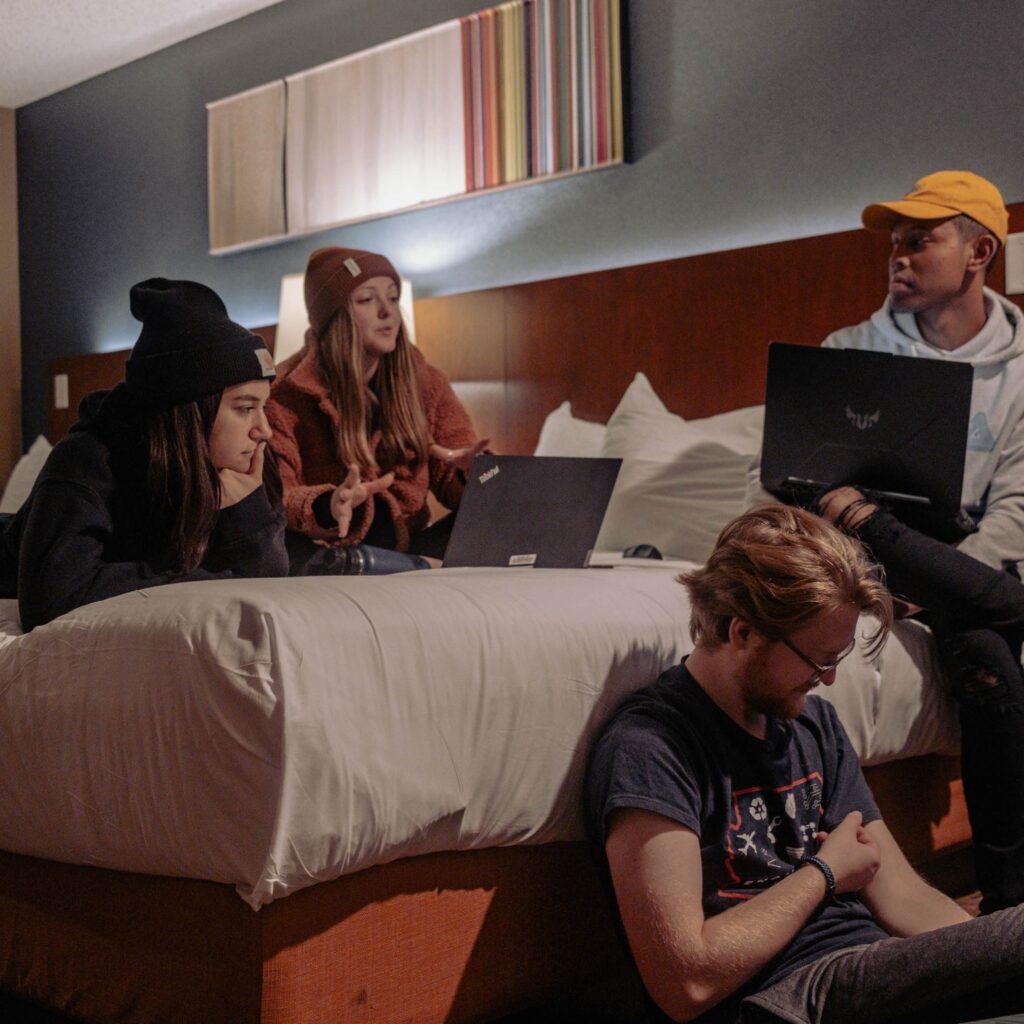 Students from Arizona team gathered together on a hotel bed to study. Two students have laptops.