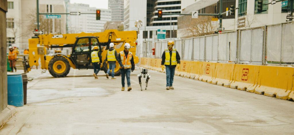 Two construction professionals walk with Leica's Robotic Integration Dog on job site