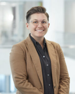 KK Clark, with short brown hair and a light brown blazer and black shirt smiling in portrait photo. ENR 20 under 40.